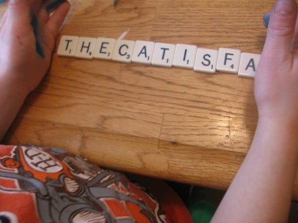 child writing words with scrabble tiles