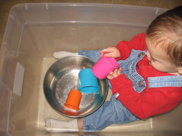 baby playing with cups in box