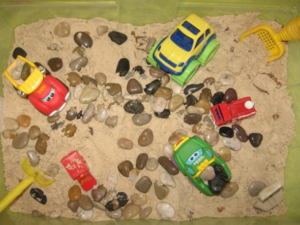 sandbox with cars, rocks, and sand toys