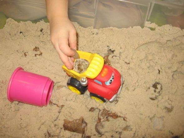 child driving toy truck in sandbox