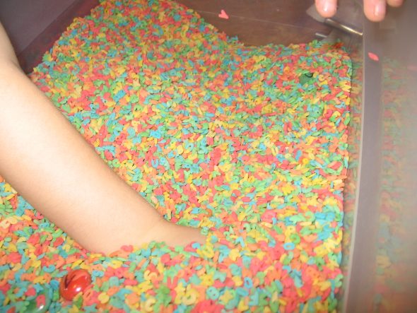 child digging in bin of colored alphabet pasta