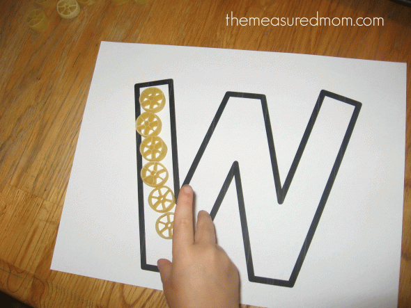 child placing wagon wheel pasta on letter W outline